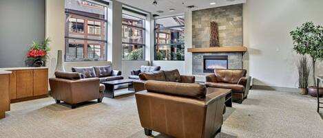 A spacious lobby with leather sofas, a fireplace, and large windows offering views of buildings.