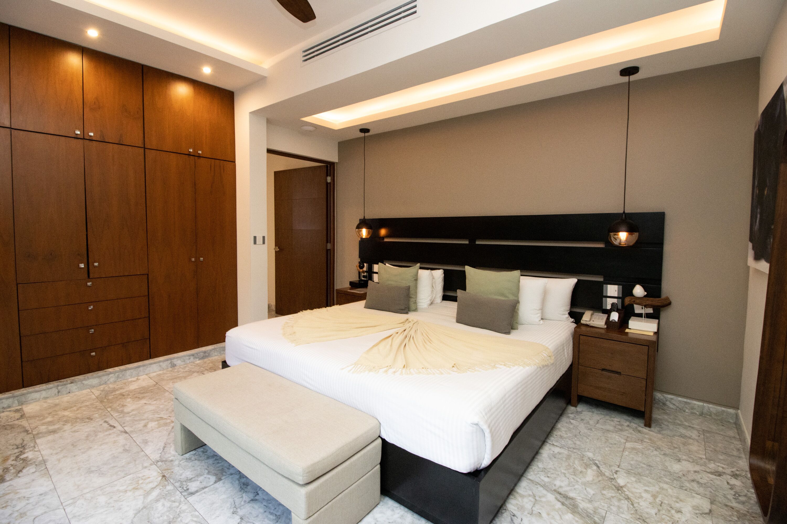 Ein modernes Schlafzimmer mit einem großen Bett, einer Sitzbank, einem Holzschrank und einem Nachttisch mit Lampe.