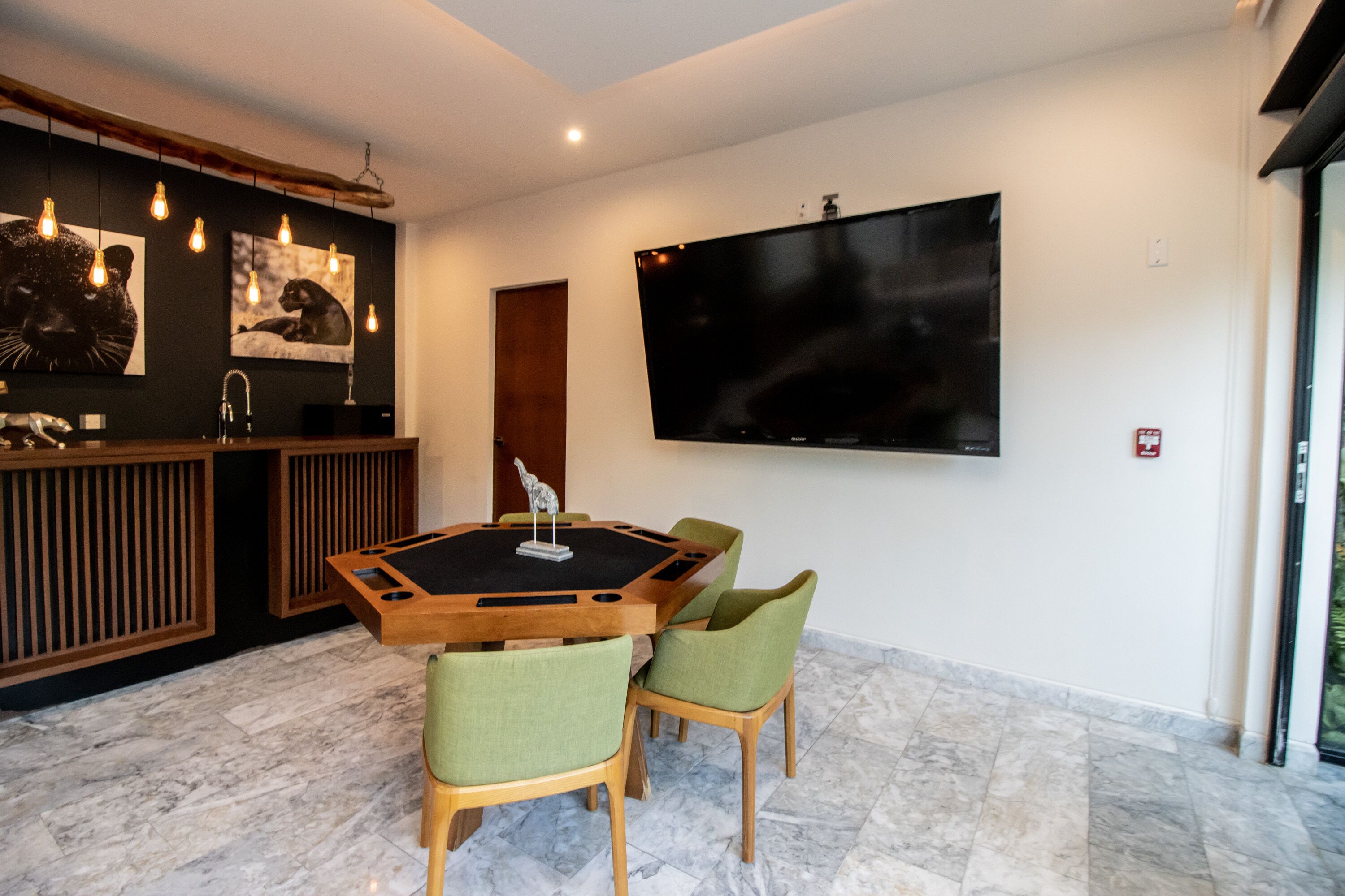 Un'area pranzo moderna con un tavolo rotondo, sedie verdi, una lavagna e un televisore a schermo piatto montato al muro.