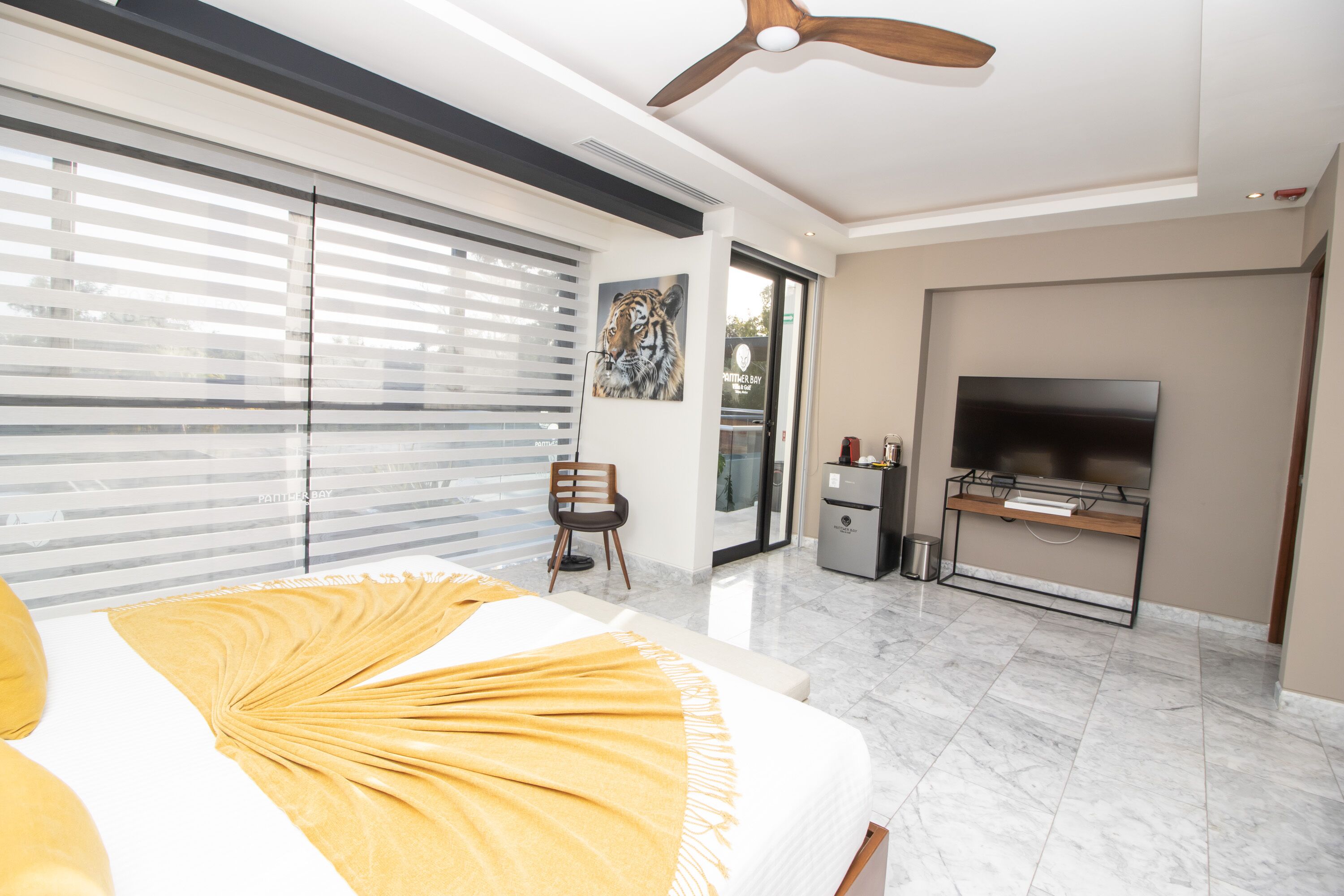 A modern bedroom with a large bed, a ceiling fan, a TV, and a sliding glass door leading to a balcony.