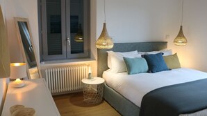 A bedroom with a bed, bedside table, lamp, and a window with blinds. - Casa Beverly 2 - My Home in Como (Argegno)