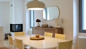 A dining area with a round table, six chairs, a hanging light fixture, a television, a mirror, and a radiator. - Casa Beverly 2 - My Home in Como (Argegno)