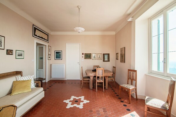 Una habitación con sofá, una mesa de comedor con sillas, un radiador y cuadros en las paredes.
