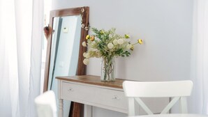 Un escritorio blanco con un florero, un espejo y una silla blanca en una habitación con piso de madera.