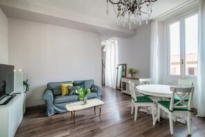 Un salon comprenant un canapé, une table basse, une table à manger avec des chaises, un lustre et une vue sur l’extérieur.