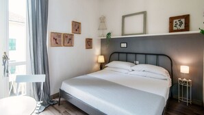 Un dormitorio con cama, lámparas de noche, cómoda, silla y obras de arte en las paredes.