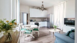 Una cocina moderna con armarios blancos, un refrigerador de acero inoxidable y un comedor con sillas blancas.