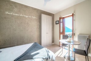 A bedroom with a bed, a small table with chairs, a wardrobe, and a view of the lake. - I Promessi Sposi - My Home in Como (Cernobbio)