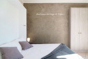 Un dormitorio con cama, almohadas, una mesita de noche con lámpara, un armario y una pared con textura.