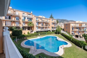 Un edificio residencial con piscina rodeado de vegetación y un cielo azul despejado.