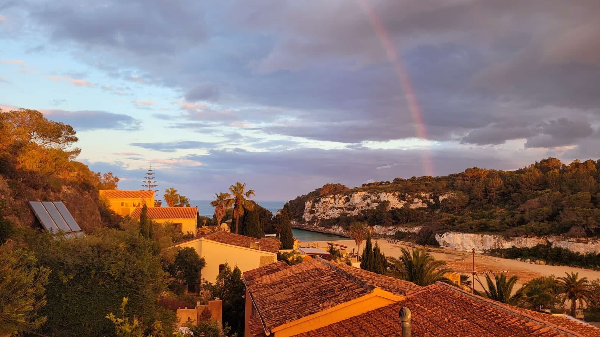 A coastal landscape with buildings, a cliff, and a rainbow.