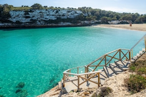 A coastal area with clear turquoise water, a sandy beach, and a wooden staircase leading down to the water.