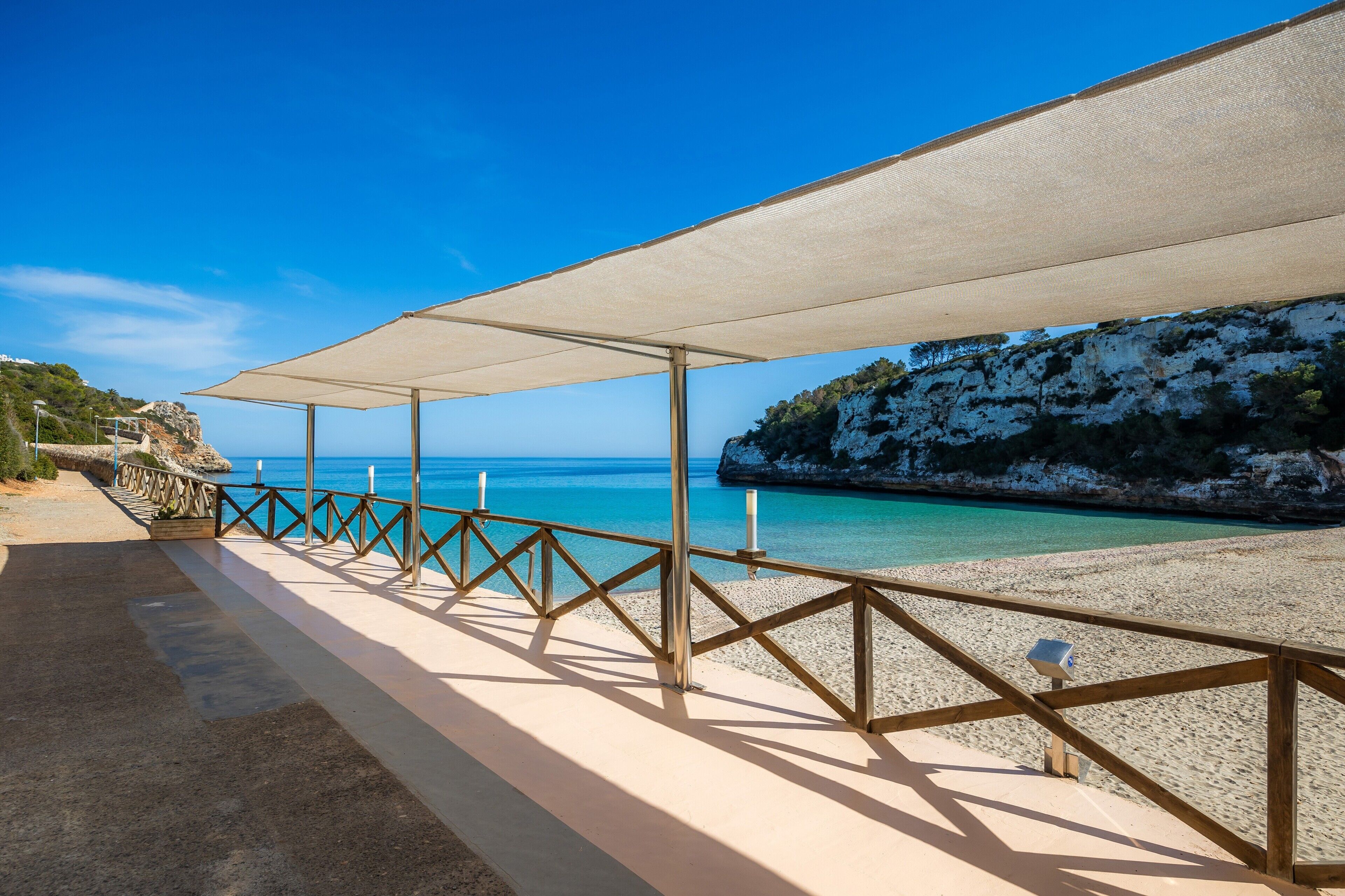 A beach with a wooden railing, a covered walkway, and a rocky cliff.