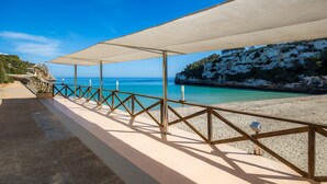 Una platja amb una barana de fusta, un passeig cobert i un penya-segat rocos.