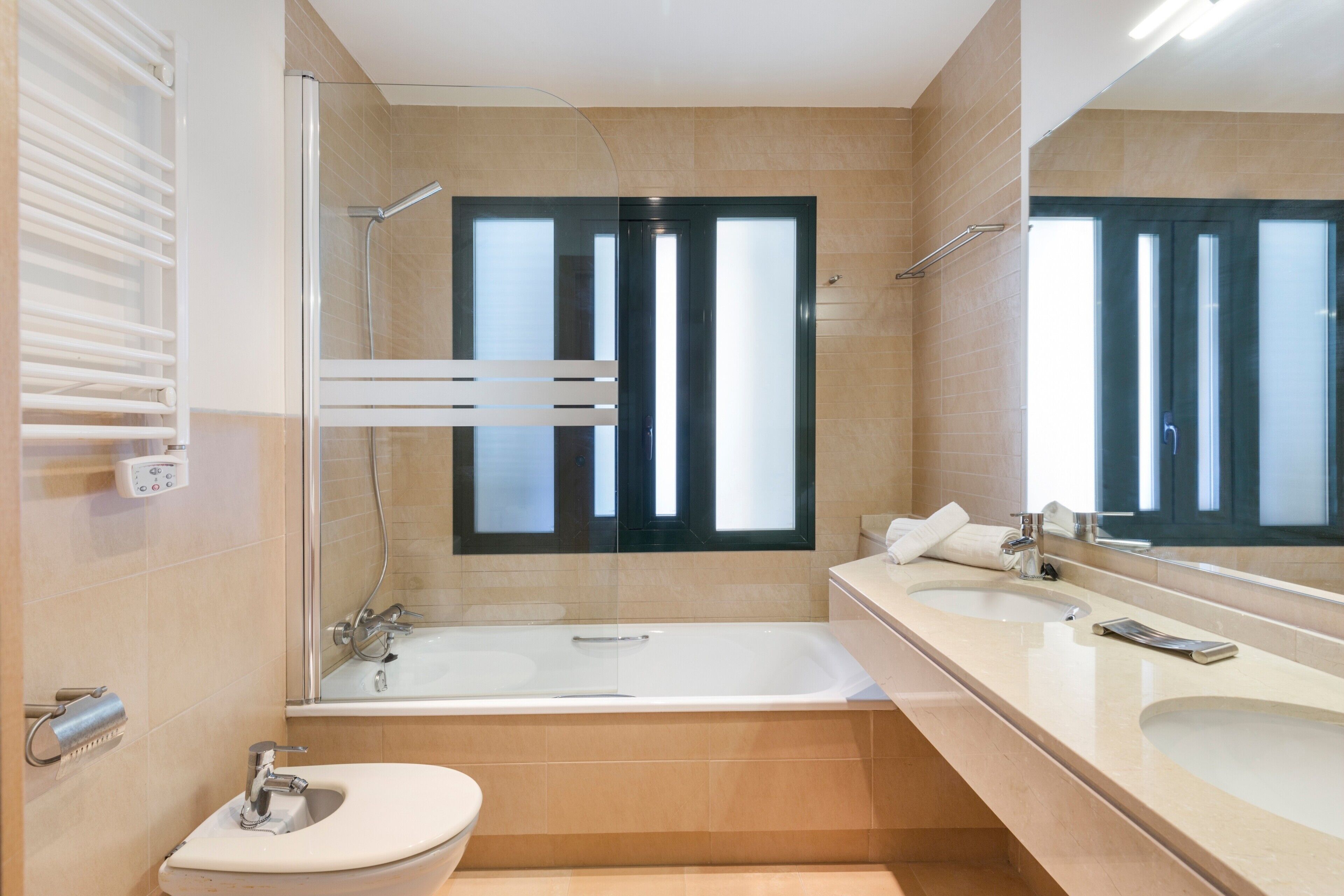 Un baño moderno con bañera, dos lavamanos, inodoro y un espejo grande.