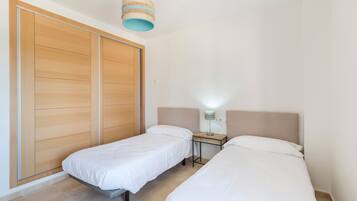 Un dormitorio con dos camas individuales, un armario de madera, una mesita de noche con lámpara y una lámpara colgante.