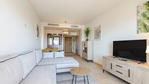 Ein modernes Wohnzimmer mit einem Ecksofa, einem Fernseher auf einer Holzkommode und einem Flur, der in einen Essbereich führt.