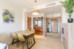 A modern dining area with a wooden table and chairs, a hanging light fixture, and a potted plant.