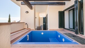 A rooftop pool with a blue interior, a wooden pergola, and a sliding glass door.