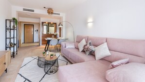 A modern living room with a pink sofa, a coffee table, and a dining area in the background.