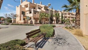 A multi-story residential building with balconies, a paved pathway, and a bench.