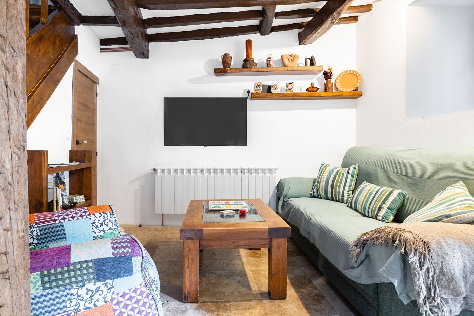 Un soggiorno accogliente con un divano verde, un tavolino in legno, una coperta trapuntata, una libreria e un televisore a parete.