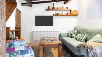 Un soggiorno accogliente con un divano verde, un tavolino in legno, una coperta trapuntata, una libreria e un televisore a parete.