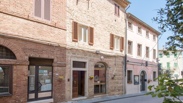 A two-story building with a brick facade, multiple doors, and windows with shutters. - 'In the Heart of Radicondoli' Apartment with Wi-Fi (Radicondoli)