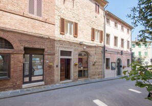 A two-story building with a brick facade, multiple doors, and windows with shutters. - 'In the Heart of Radicondoli' Apartment with Wi-Fi (Radicondoli)