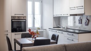 A modern kitchen with white cabinets, a built-in oven, and a dining area with a table and chairs. - 'In the Heart of Radicondoli' Apartment with Wi-Fi (Radicondoli)