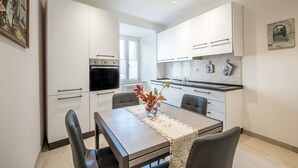 A modern kitchen with white cabinets, a dining table with chairs, and a vase with flowers. - 'In the Heart of Radicondoli' Apartment with Wi-Fi (Radicondoli)