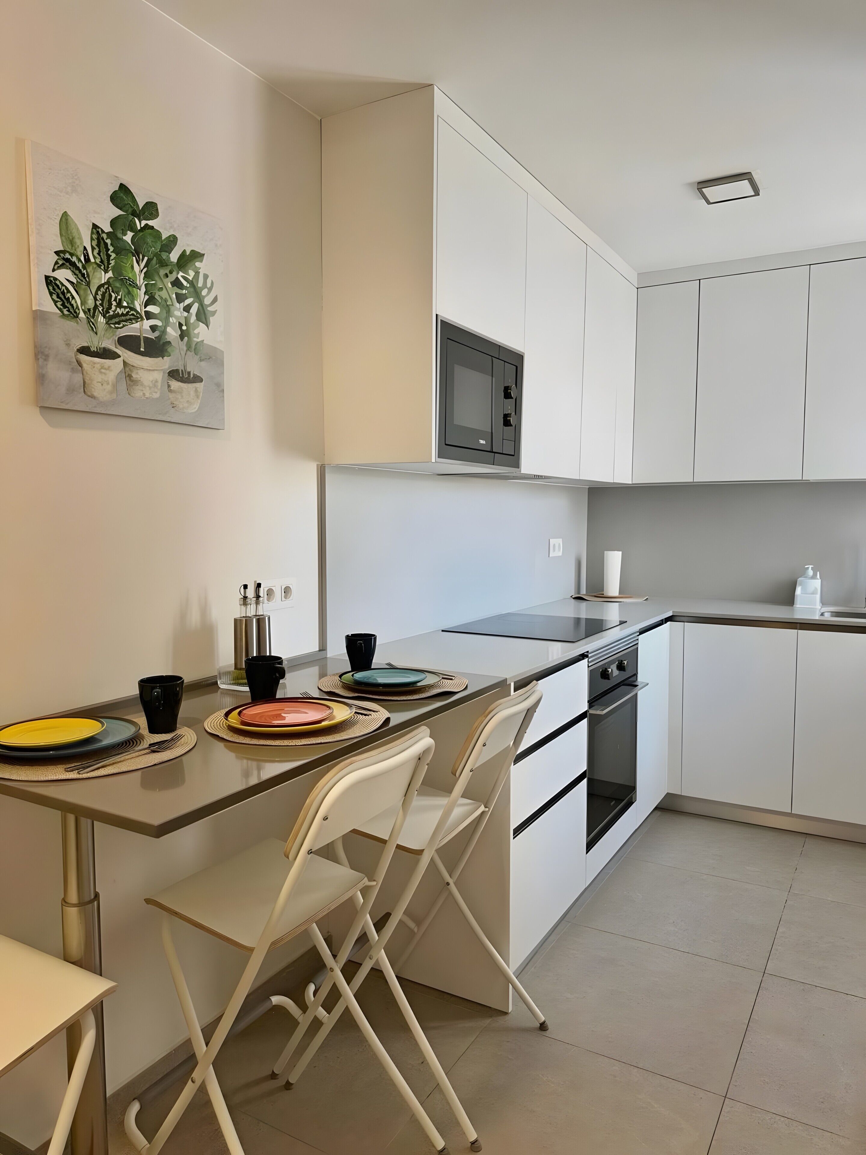 Une cuisine moderne avec des meubles blancs, un four à micro-ondes, une cuisinière et un coin repas équipé de chaises et d’assiettes.