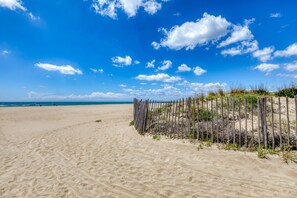 A sandy beach with a wooden fence and sparse vegetation.