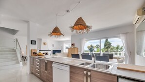Una cocina moderna con una isla central, pileta de acero inoxidable e iluminación colgante de fibras naturales.