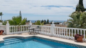 Una piscina con barandilla blanca, una mesa y sillas, y vista al mar.