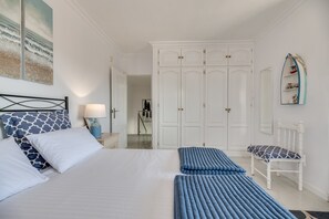 Une chambre à coucher comprenant un lit, des oreillers, un banc, une table de chevet, une lampe, une armoire et un miroir.