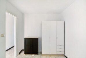 Una habitación con un armario blanco, un pequeño mueble negro y una puerta que da a otra habitación.