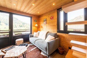 Un intérieur en bois avec un canapé, une table sur laquelle se trouve un plateau, une lampe et une vue sur l’extérieur.