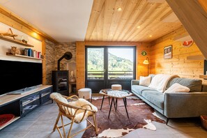 Una sala de estar acogedora con chimenea, un sofá, un televisor y un amplio ventanal con vistas al exterior.