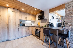 Une cuisine moderne avec des meubles en bois, un four encastré et un coin bar avec des tabourets.