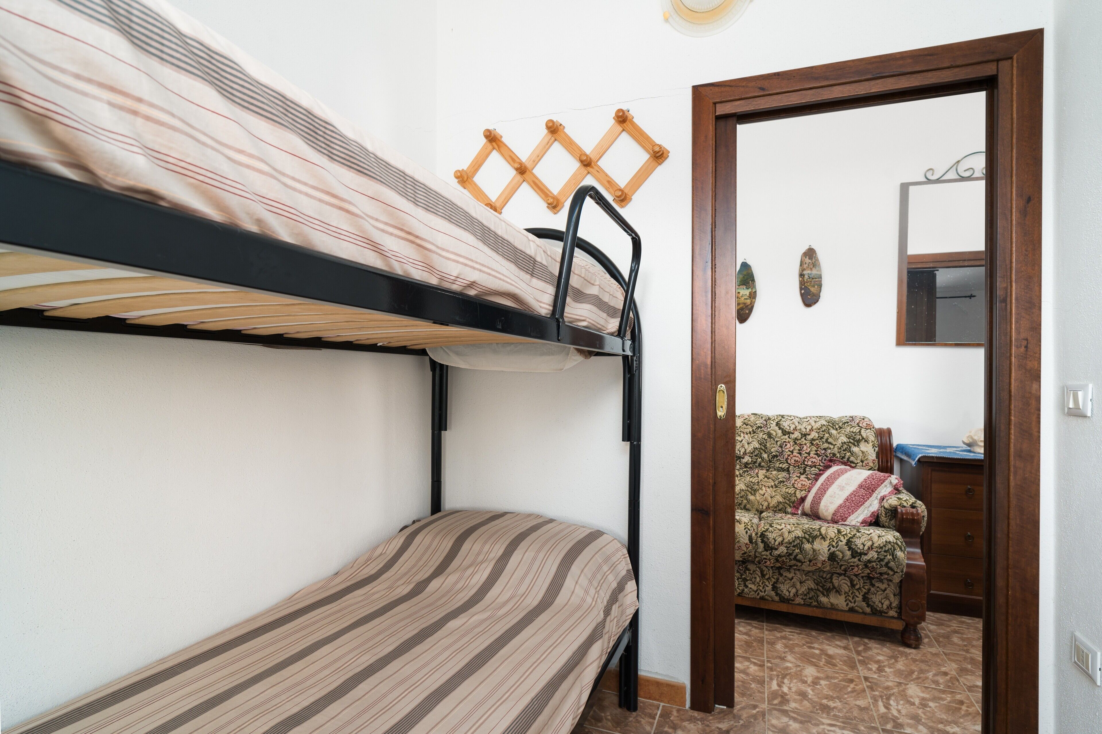 A bunk bed with a striped mattress, a wooden door, a floral sofa, and a small table with a blue cover.