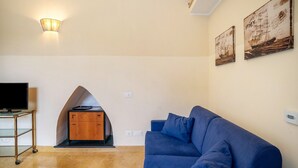 A living room with a blue sofa, a TV on a stand, a wooden cabinet, and two wall-mounted paintings.