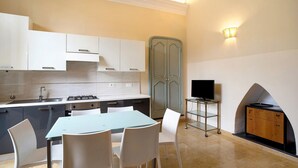 A modern kitchen with white cabinets, a dining table with chairs, a TV on a stand, and a fireplace.