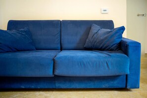 A blue sofa with two pillows against a wall with a thermostat. - Apartment 'Conchiglia, Borgo Dei Pescatori (Cervo)