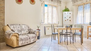A living room with a sofa, a dining table with chairs, a radiator, and a window with curtains. - Holiday Apartment "Casa Laureta" with Private Terrace & Wi-Fi (Piombino)