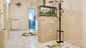 A reception area with a stone wall, a fish tank, a coat rack, and a geometric rug. - Holiday Apartment "Casa Laureta" with Private Terrace & Wi-Fi (Piombino)