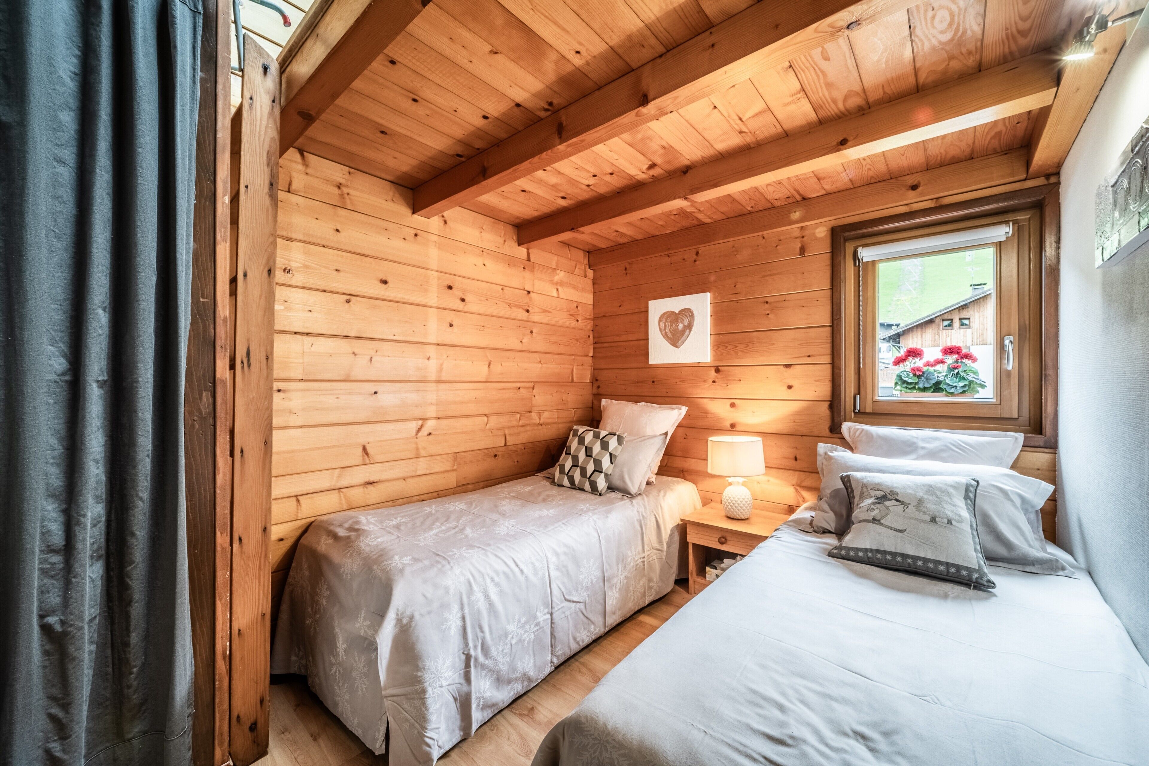 Een slaapkamer in een houten chalet met twee bedden, een raam met uitzicht en een hartvormige decoratie aan de muur.
