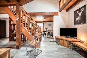 Un vaste espace de vie agrémenté d’un escalier en bois, d’un téléviseur et d’un tableau représentant un cerf, accroché au mur.