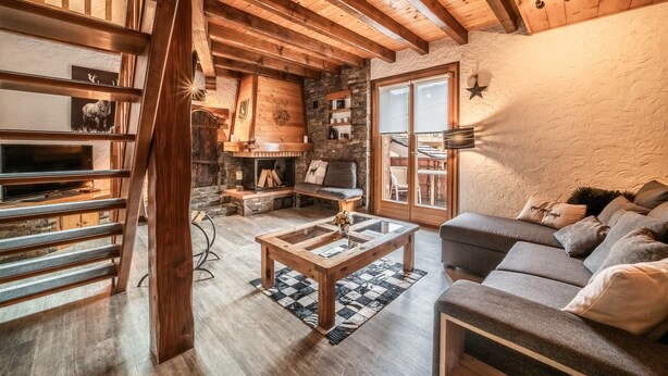 Een rustiek interieur met zichtbare houten balken, een stenen openhaard, een bank en een glazen bijzettafeltje.
