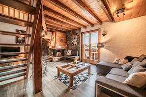 Un intérieur rustique avec des poutres apparentes, une cheminée en pierre, un canapé et une table basse en verre.
